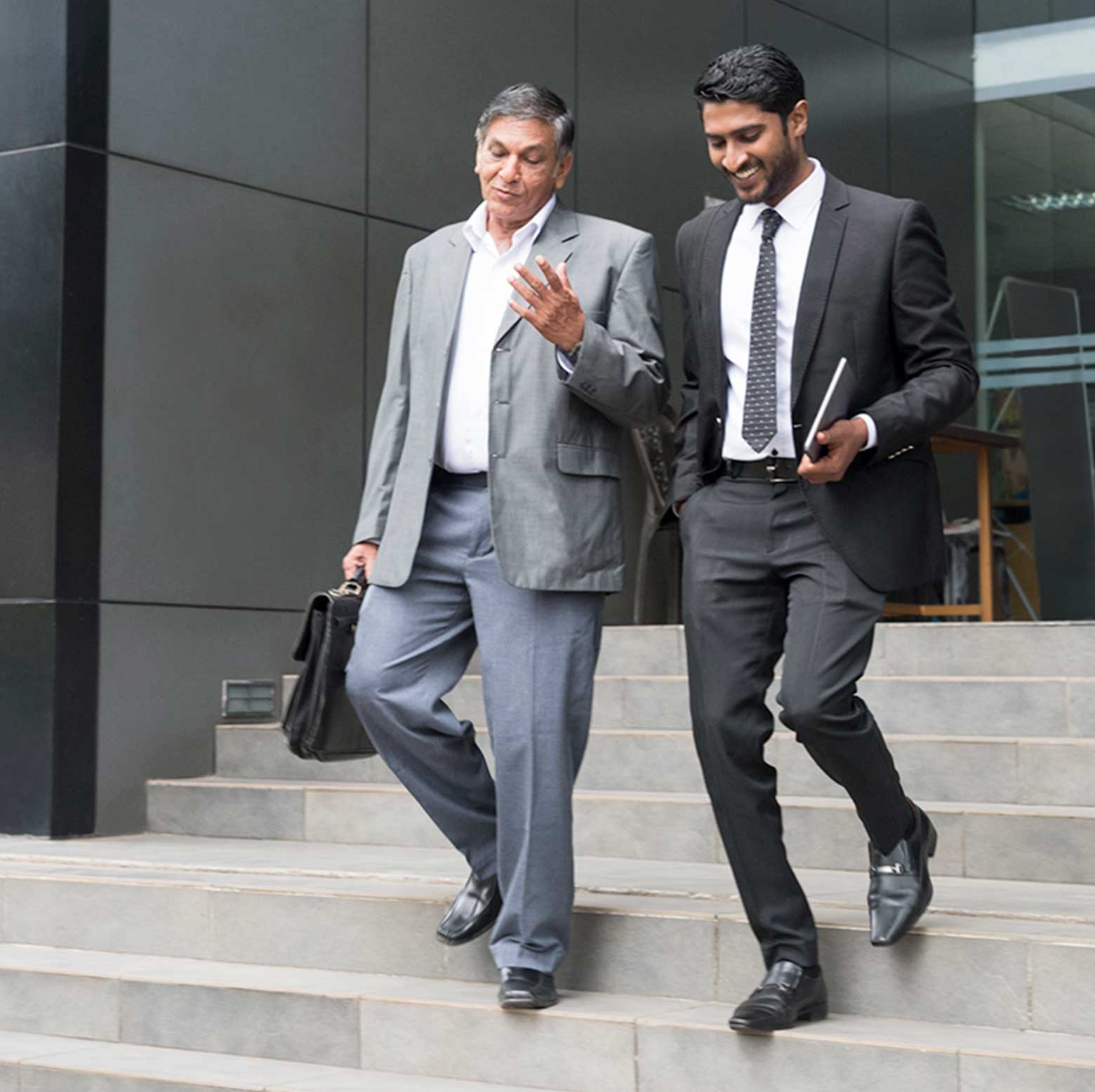 Two male business colleagues wearing suits and walking down the stairs outside an office building
